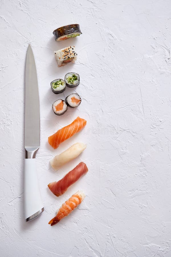 Various sushi rolls with Japanese knife on white stone slate background royalty free stock image Various sushi rolls with Japanese knife on white stone slate background royalty free stock image