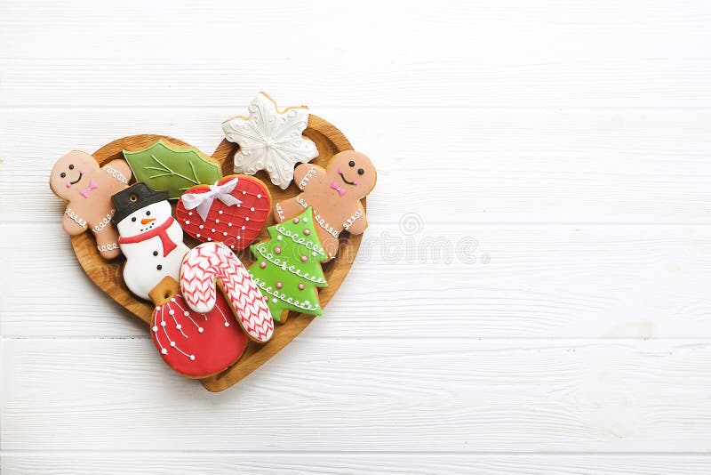 Various types of Christmas decorative gingerbread cookies on wooden heart shaped plate on white table top view, text space
