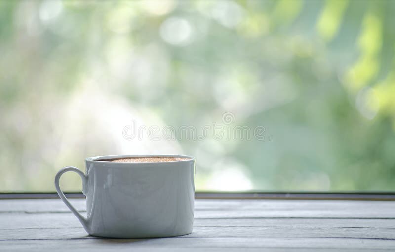 Varm kaffekopp med vitt trätabellen och den gröna bladbakgrunden med kopieringsutrymme på rätt royaltyfri bild Varm kaffekopp med vitt trätabellen och den gröna bladbakgrunden med kopieringsutrymme på rätt royaltyfri bild