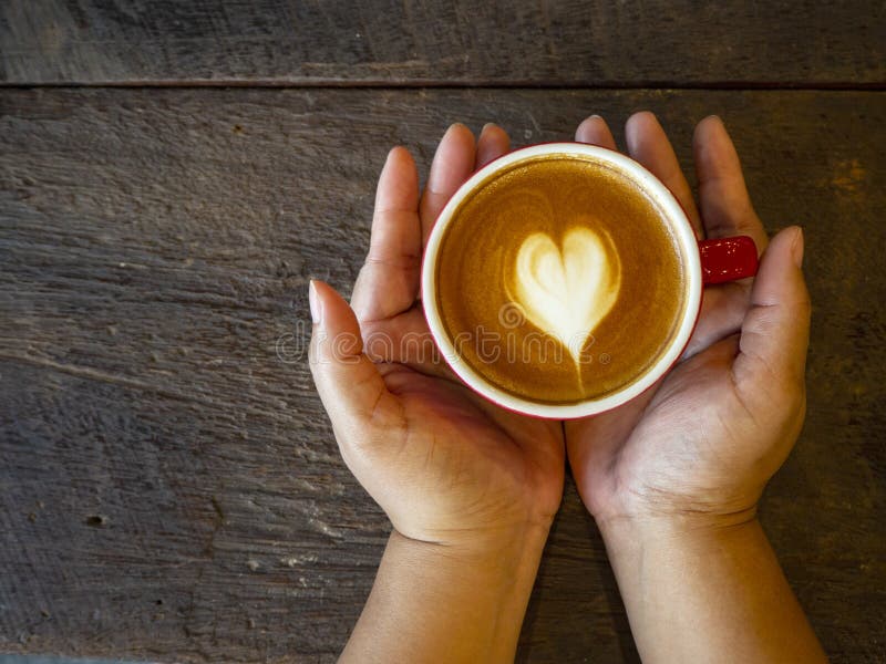 Varm lattekonst på trätabellen. Kvinnainnehav i handkopp kaffe på mörkt träbegrepp för bakgrundsvalentinförälskelse