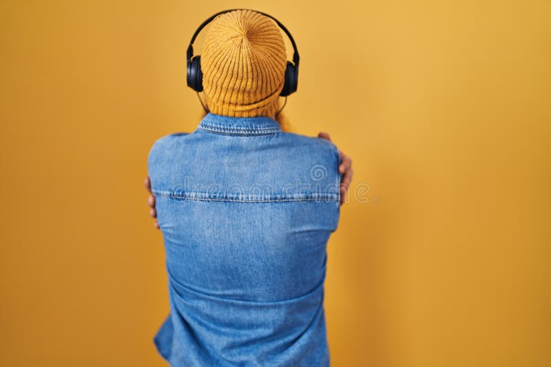 Varsam man med långt skägg som lyssnar på musik med hörlurar som kramar sig själv glada och positiva bakifrån arkivbild