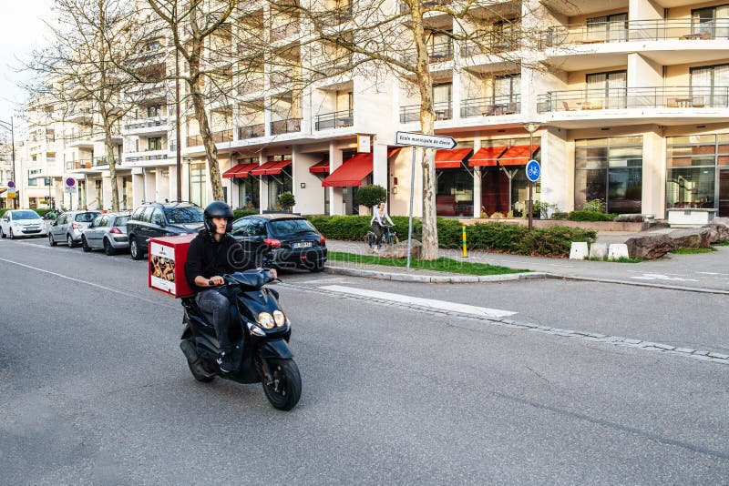 Varón en la vespa en las calles de Estrasburgo que entregan el sushi fotografía de archivo Varón en la vespa en las calles de Estrasburgo que entregan el sushi fotografía de archivo