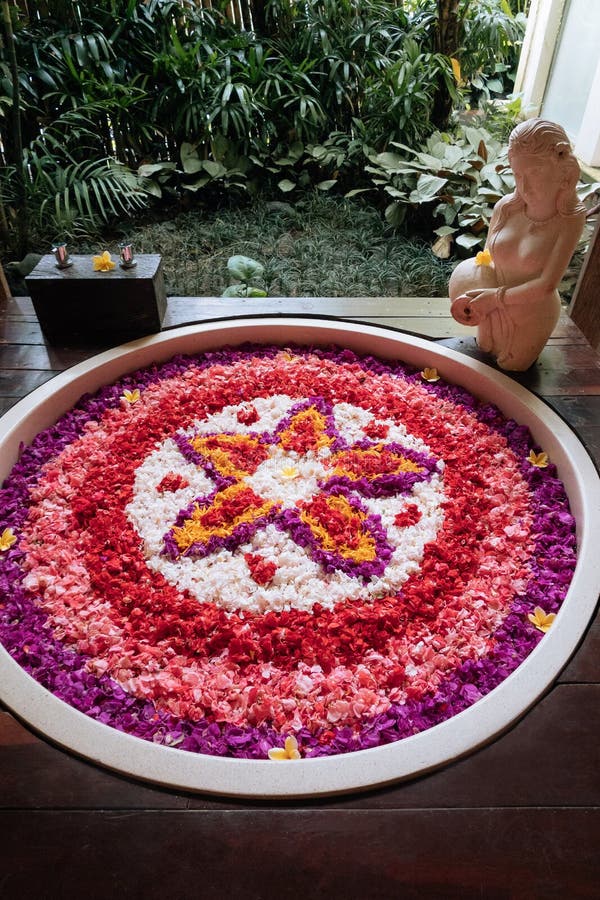 Vasca da bagno in pietra con petali di fiori a forma di cuore vicino alla  finestra con vista sulla giungla. Relax spa biologica nel lussuoso bagno di  Bali . - Foto Stock