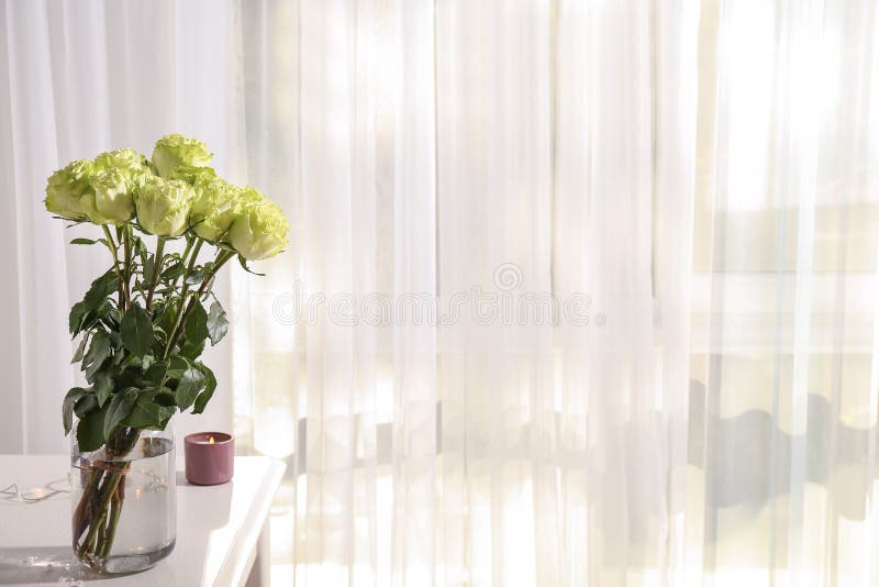 Vase with beautiful green roses on white table in room