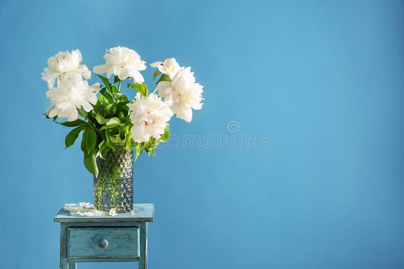 Vase with beautiful peony flowers on table against color background stock photo Vase with beautiful peony flowers on table against color background stock photo