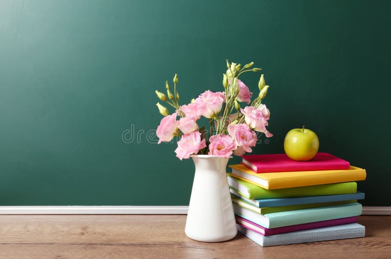 Vase of flowers, books and apple on wooden table near green chalkboard, space for text