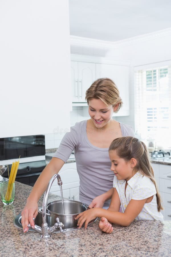Vaso di riempimento della figlia e della madre con acqua fotografia stock Vaso di riempimento della figlia e della madre con acqua fotografia stock