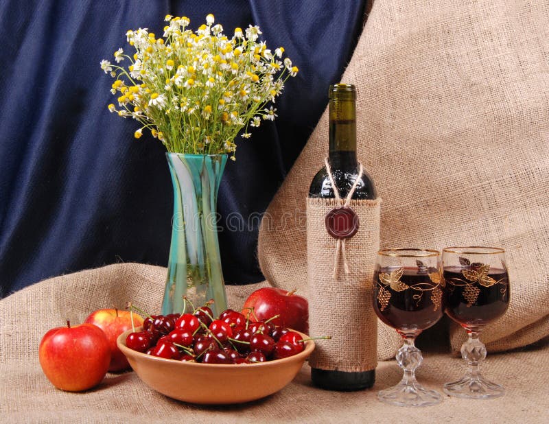 Still life, glass vase with flowers (camomiles), apples, cherry, wine and wineglass on blue background with sacking. Still life, glass vase with flowers (camomiles), apples, cherry, wine and wineglass on blue background with sacking