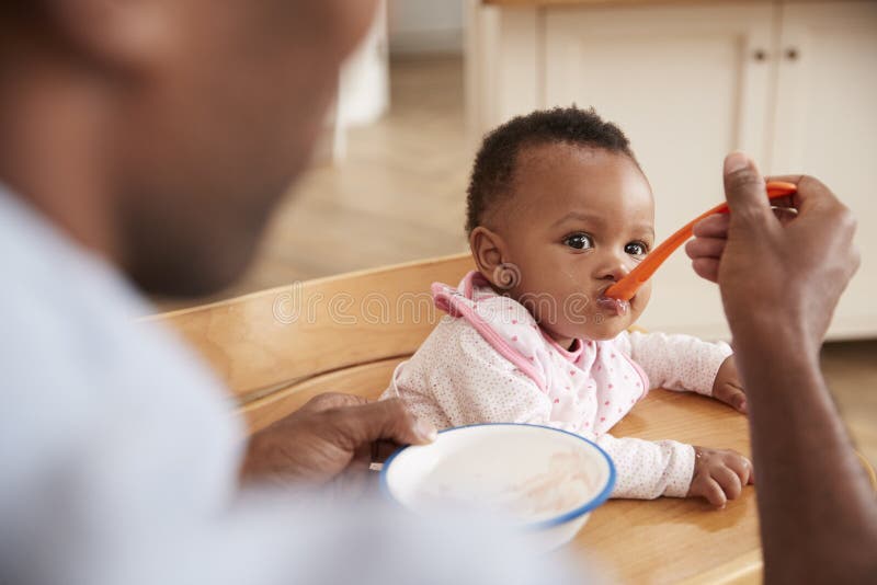 Vater Feeding Baby Daughter im Hochstuhl stockfotografie Vater Feeding Baby Daughter im Hochstuhl stockfotografie