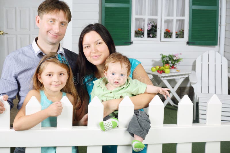 Vater, Mutter, Baby und Tochter stehen nahe bei weißem Zaun lizenzfreie stockbilder Vater, Mutter, Baby und Tochter stehen nahe bei weißem Zaun lizenzfreie stockbilder