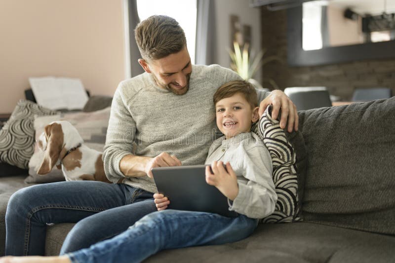 Vater oder Pate mit Basset Hund, die sich im Wohnzimmer mit Computertablette amüsieren lizenzfreies stockbild
