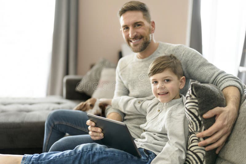 Vater oder Pate mit Basset Hund, die sich im Wohnzimmer mit Computertablette amüsieren stockfotos