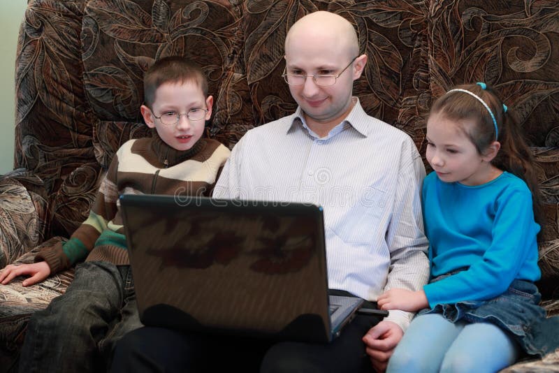 Vater-, Sohn- und Tochtersitzen betrachten Laptop lizenzfreies stockbild Vater-, Sohn- und Tochtersitzen betrachten Laptop lizenzfreies stockbild