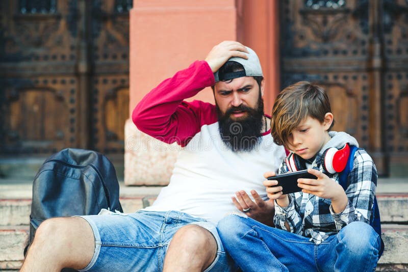 Vater und Sohn benutzen Smartphones Papa und Sohn verbringen gemeinsam im Freien Teenager, der telefonisch Spiele spielt Muttersc lizenzfreie stockfotos Vater und Sohn benutzen Smartphones Papa und Sohn verbringen gemeinsam im Freien Teenager, der telefonisch Spiele spielt Muttersc lizenzfreie stockfotos