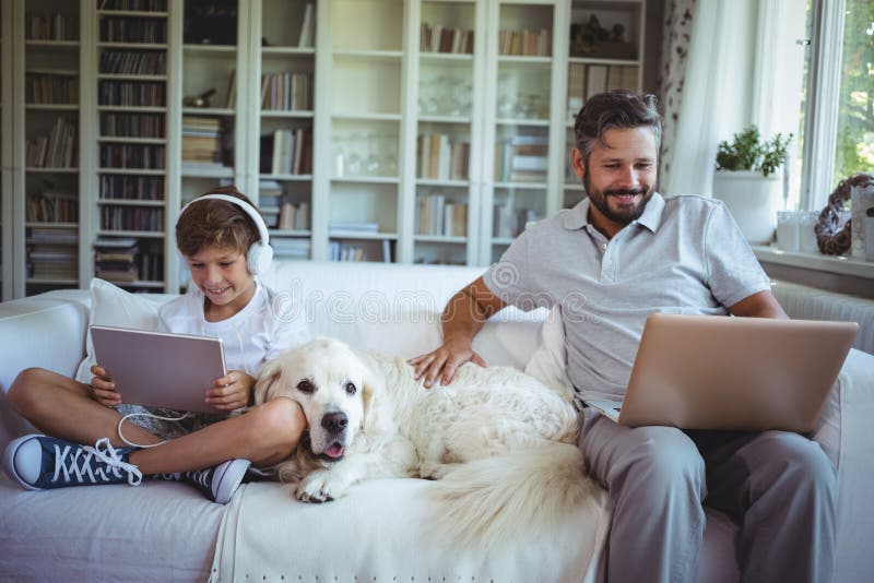 Vater und Sohn, die auf Sofa sitzen und digitale Tablette und Laptop verwenden lizenzfreies stockfoto Vater und Sohn, die auf Sofa sitzen und digitale Tablette und Laptop verwenden lizenzfreies stockfoto