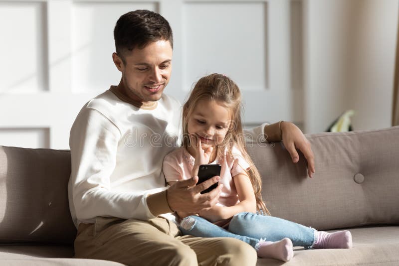 Vati und Kind sitzen auf der Couch mithilfe des Smartphonegerätes lizenzfreie stockbilder