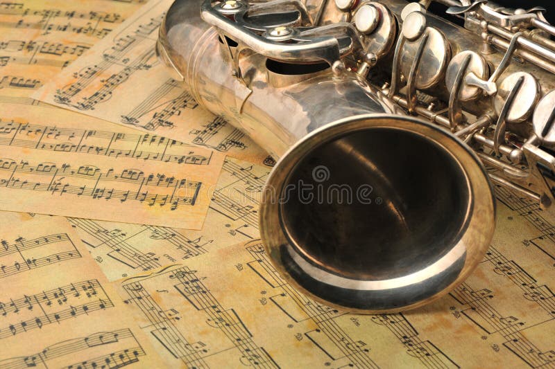 Old saxophone and notes. The Musical instrument laying on notes with classical music of the beginning of 17 centuries. Old saxophone and notes. The Musical instrument laying on notes with classical music of the beginning of 17 centuries