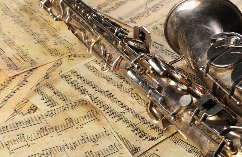 Old saxophone and notes. The Musical instrument laying on notes with classical music of the beginning of 17 centuries. Old saxophone and notes. The Musical instrument laying on notes with classical music of the beginning of 17 centuries