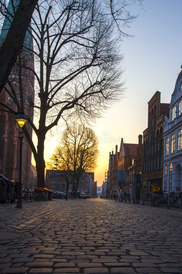 Vecchia città con le vie e gli alberi cobbled in Europa al tramonto immagine stock Vecchia città con le vie e gli alberi cobbled in Europa al tramonto immagine stock