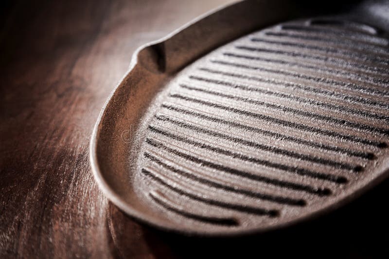 Old cast iron griddle pan for roasting and grilling in a close up angled view on a rustic wooden table. Old cast iron griddle pan for roasting and grilling in a close up angled view on a rustic wooden table