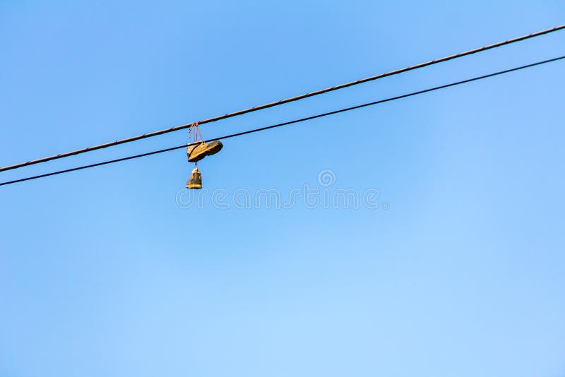 Vecchie scarpe da tennis che appendono sul cavo elettrico con cielo blu nei precedenti immagini stock Vecchie scarpe da tennis che appendono sul cavo elettrico con cielo blu nei precedenti immagini stock