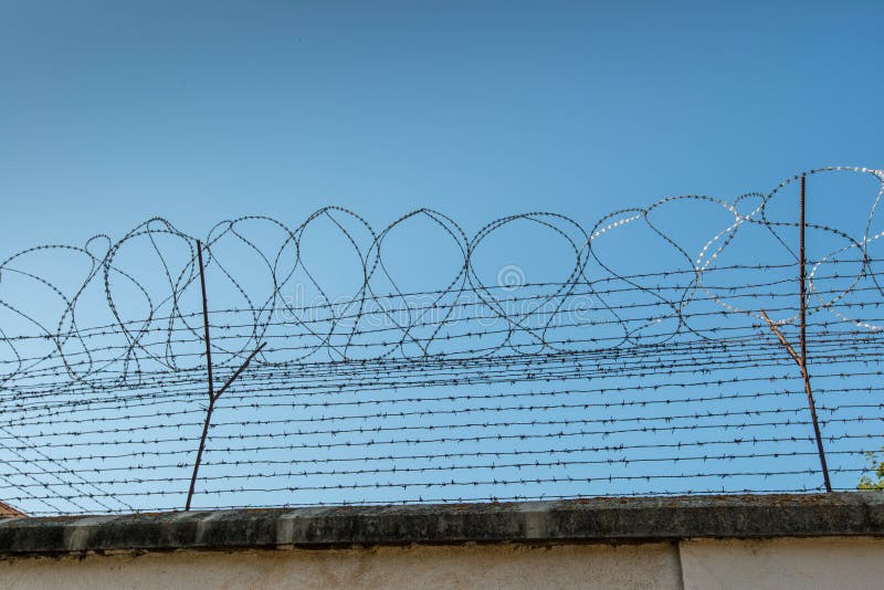 Vedação com fio barrado na parede da prisão contra o céu azul perfeito
