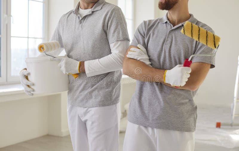 Vedere decupată a pictorilor masculi fără față care țin cupe și role pentru vopsele ocupate pentru renovare stock photo