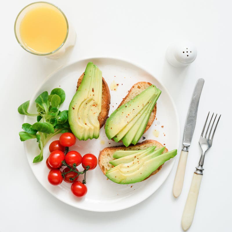 Vegan avocado toasts and orange juice on white plate, top view