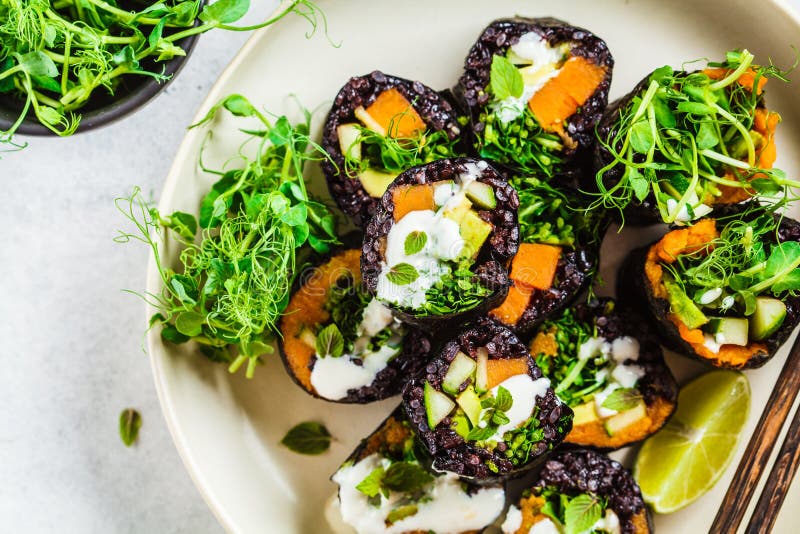 Vegan sushi rolt met zwarte rijst, avocado en zoete aardappel op een witte schaal, bovenaanzicht Vegaans voedselconcept