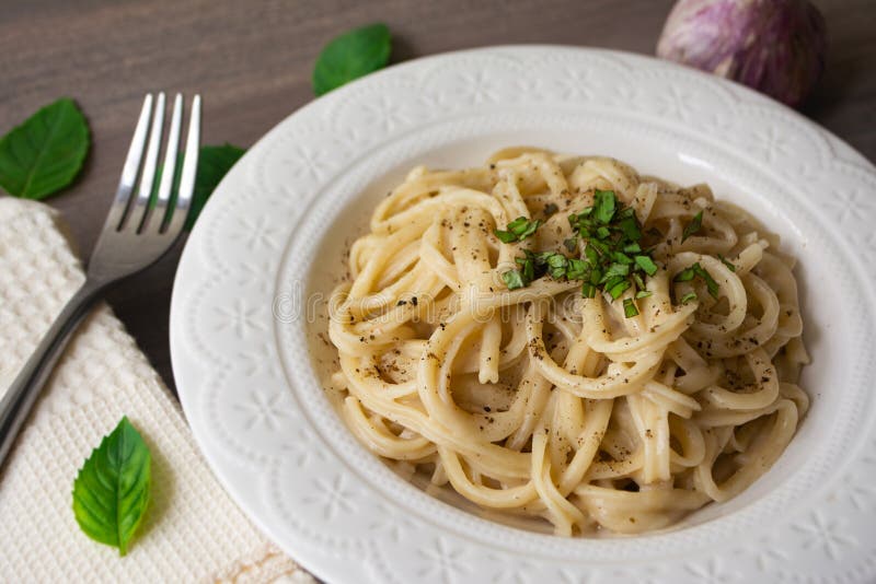 Vegan version of traditional italian pasta fettuccine alfredo with creamy white sauce garnished with basil. On a wooden surface with a fork, napkin, garlic and stock images