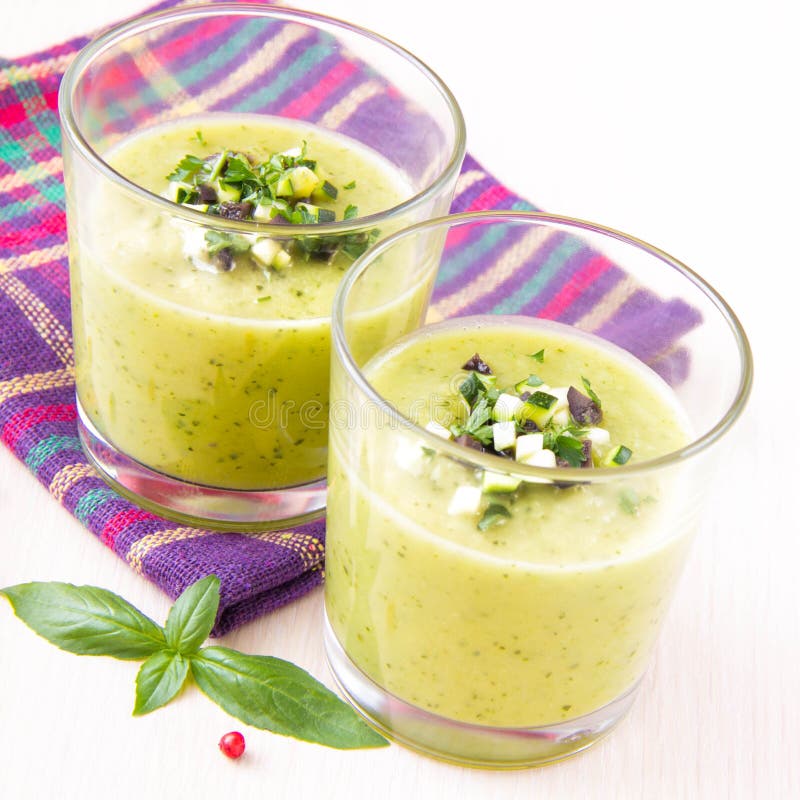 Vegetable cream soup with avocado, herbs, zucchini and black olives in glasses as an snack