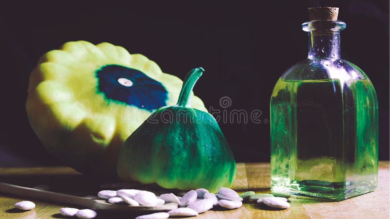 Vegetable oil next to pumpkin seeds on a rustic wooden table against a black cloth background. Empty copy space for Editor`s text.