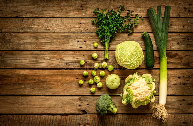 Green vegetables on vintage rustic wooden background. Rural kitchen table - flat lay composition from above, top view. Layout with free text space. Green vegetables on vintage rustic wooden background. Rural kitchen table - flat lay composition from above, top view. Layout with free text space.