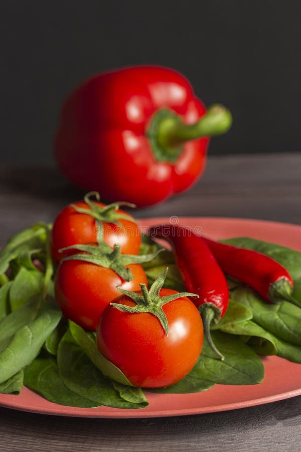 Vegetais vermelhos apetitosos três tomates com folhas, pimentas de pimentão encarnados, paprika e as folhas verdes dos espinafres imagem de stock Vegetais vermelhos apetitosos três tomates com folhas, pimentas de pimentão encarnados, paprika e as folhas verdes dos espinafres imagem de stock