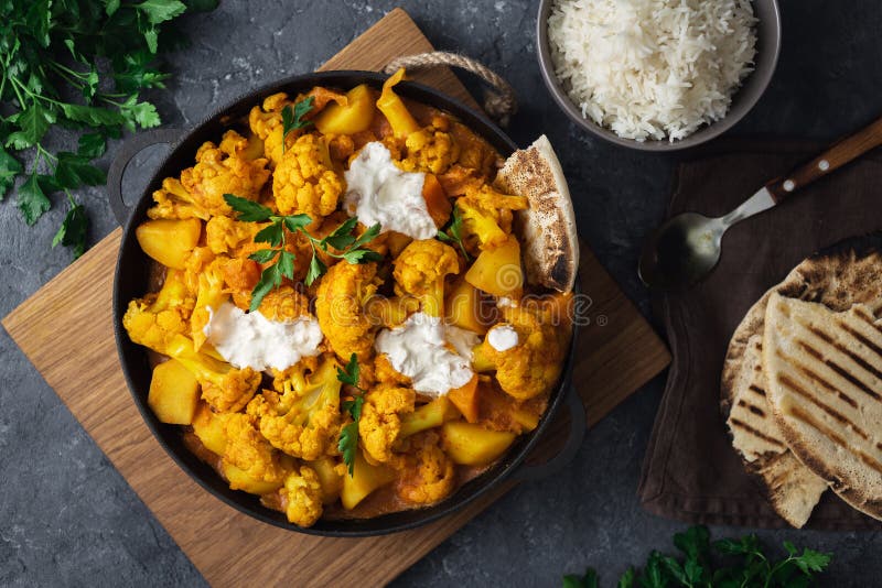 Vegetarian indian food. Cauliflower curry with basmati rice and naan bread on dark stone background top view. Healthy and tasty food concept. Vegetarian indian food. Cauliflower curry with basmati rice and naan bread on dark stone background top view. Healthy and tasty food concept