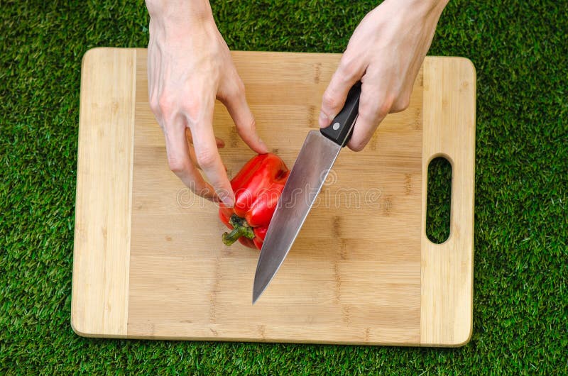 Vegetarians and cooking on the nature of the theme: human hand holding a red pepper and a knife on a cutting board and a backgroun