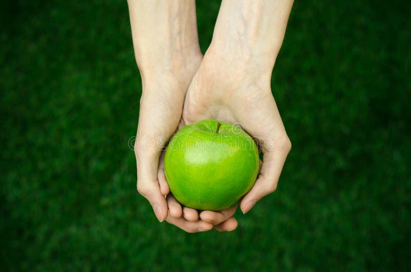 Vegetarians and fresh fruit and vegetables on the nature of the theme: human hand holding a green apple on a background of green g