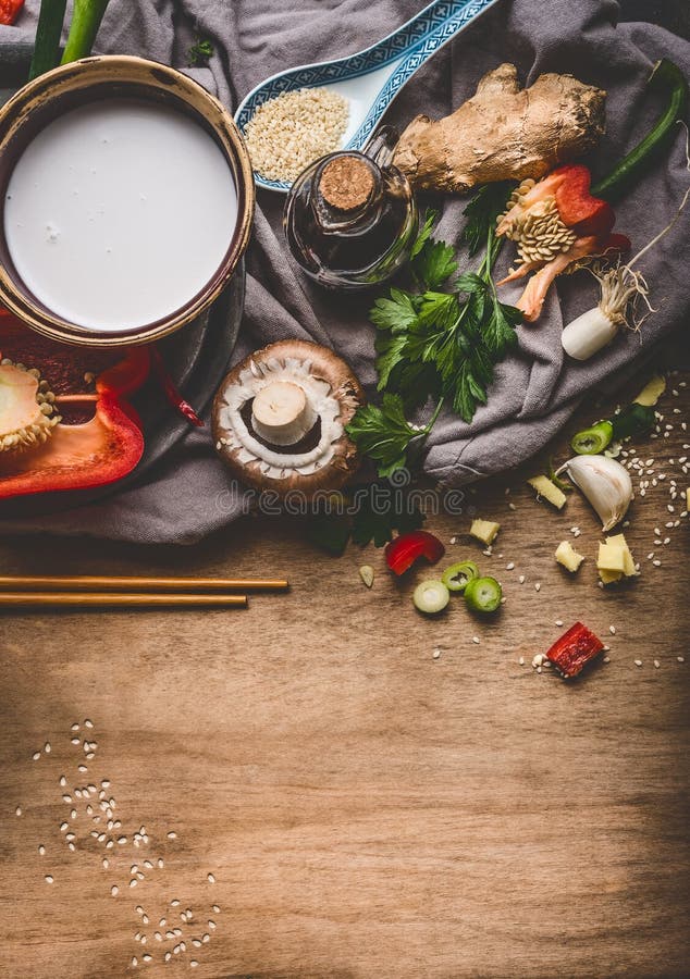 Vegetarische asiatische Küchebestandteile mit gehacktem Gemüse, Kokosmilch, Samen, Gewürzen und Essstäbchen auf rustikalem hölzer stockfotografie