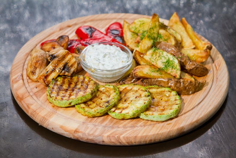 Vegetarischer Grill mit Zucchini, Pommes-Frites, Pilzen, Paprika, weißer Soße und Dill auf hölzerner Platte, Lebensmittelfoto lizenzfreie stockfotos Vegetarischer Grill mit Zucchini, Pommes-Frites, Pilzen, Paprika, weißer Soße und Dill auf hölzerner Platte, Lebensmittelfoto lizenzfreie stockfotos