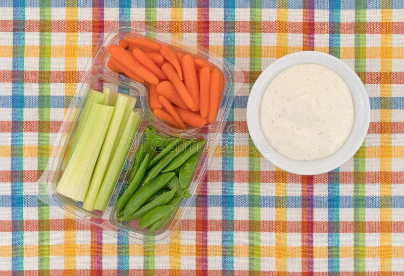 Veggies in a container with ranch dressing to the side. Top view of celery, carrots and sugar snap peas in a plastic container with a bowl of ranch dressing to stock photography