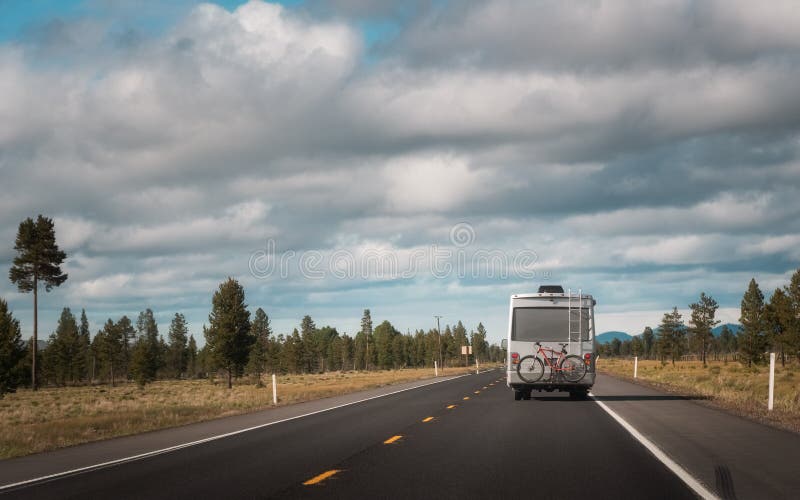 Recreational vehicle or RV or Travel van with bike hanging on the rear driving through the countryside. Travel and wanderlust concept image with copy space. Recreational vehicle or RV or Travel van with bike hanging on the rear driving through the countryside. Travel and wanderlust concept image with copy space
