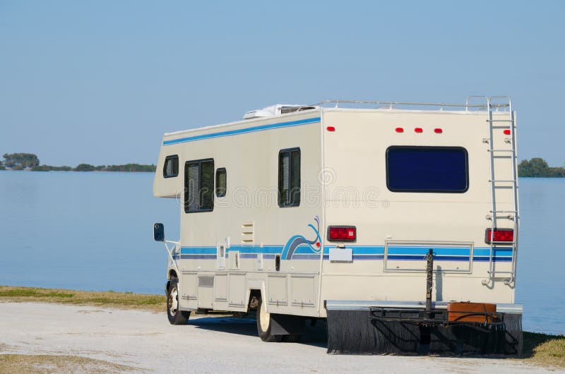 A RV recreational vehicle parked by edge of water at beautiful beach on a bright sunny blue sky day. A RV recreational vehicle parked by edge of water at beautiful beach on a bright sunny blue sky day