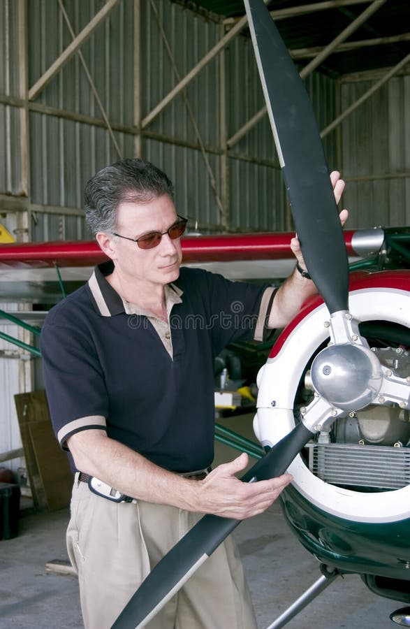 A man standing with his hands on the propeller of a small single engine plane. A man standing with his hands on the propeller of a small single engine plane.