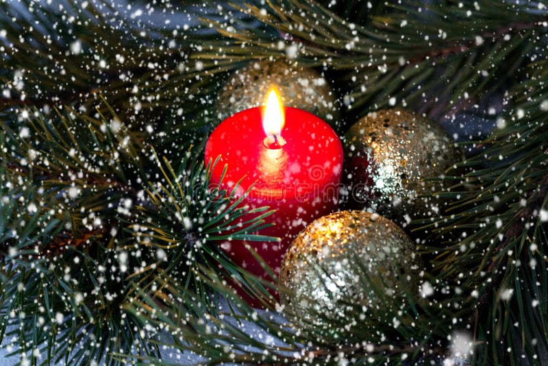 A vela ardente vermelha e as bolas douradas do Natal com um abeto ramificam sob a neve indo imagem de stock A vela ardente vermelha e as bolas douradas do Natal com um abeto ramificam sob a neve indo imagem de stock