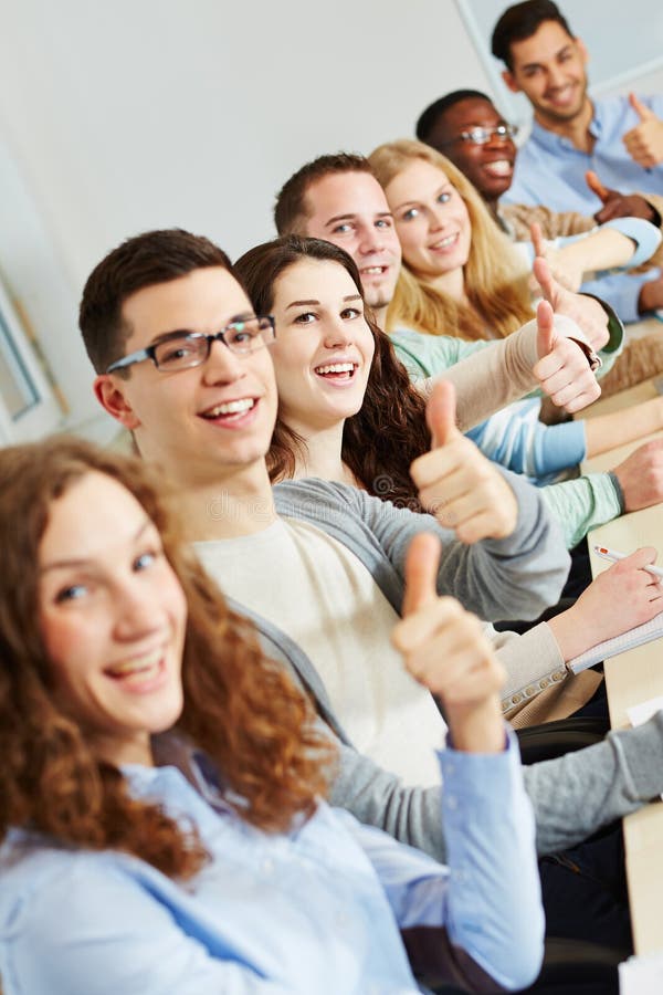 Many happy successful students holding their thumbs up in class. Many happy successful students holding their thumbs up in class