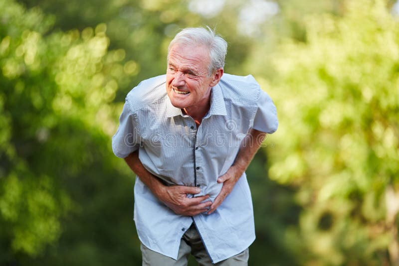 Old man with stomach ache holding his stomach in nature. Old man with stomach ache holding his stomach in nature