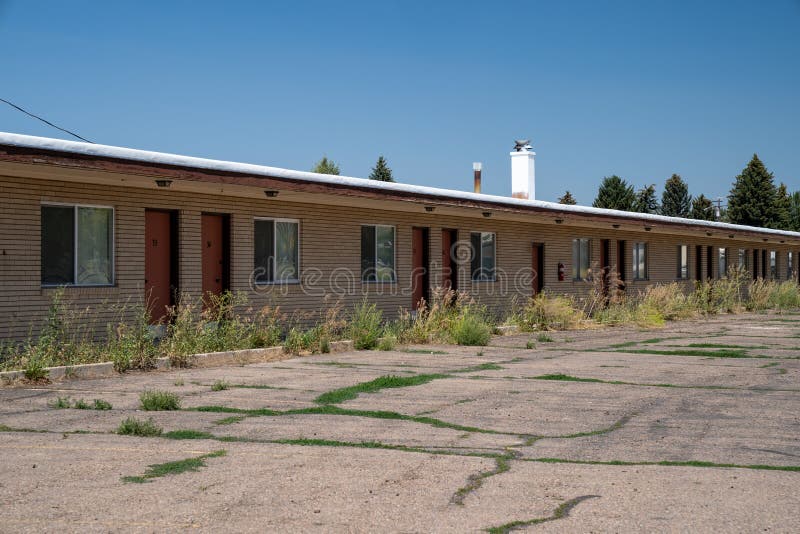 Velho motel de corte rápido abandonado decai ao sol. ervas daninhas superficiais no estacionamento