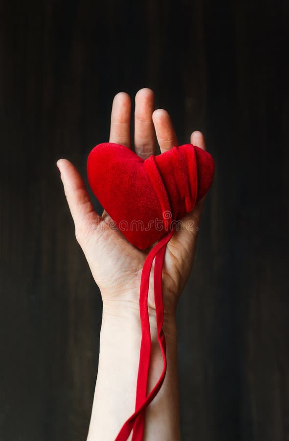 Velluto cuore rosso mano da medio vecchio una donna sul buio di legno, selettivo concentrarsi.