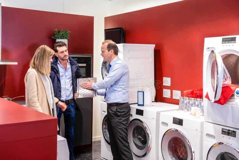 Salesman explaining product to couple in washing machine department at electronics shop. Salesman explaining product to couple in washing machine department at electronics shop