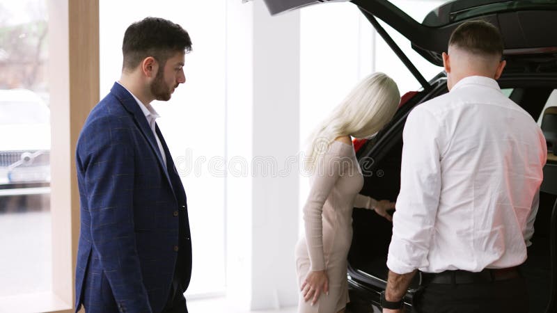 Vendedor que muestra la capacidad de un maletero desde adentro a los clientes en la vista lateral de la sala de exposición de coch metrajes